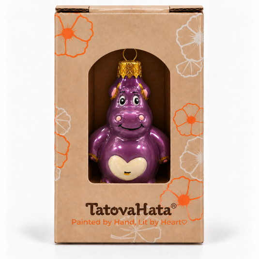 A purple hippo-shaped ornament in its original kraft paper packaging box, featuring orange and white floral designs and the brand name 'TatovaHata' printed at the bottom.