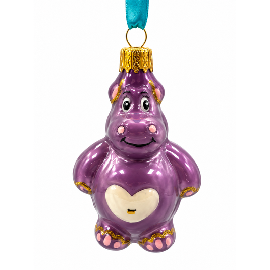 A purple hippo-shaped Christmas ornament, featuring a cream-colored heart on its belly, gold trim, and a teal hanging ribbon.